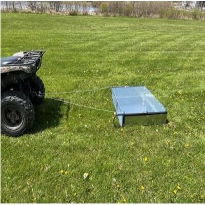 ATV pulling a metal box across a grassy field