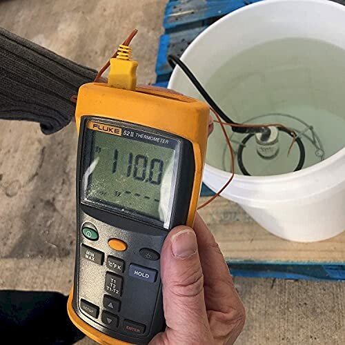 Digital thermometer measuring water temperature in a bucket.